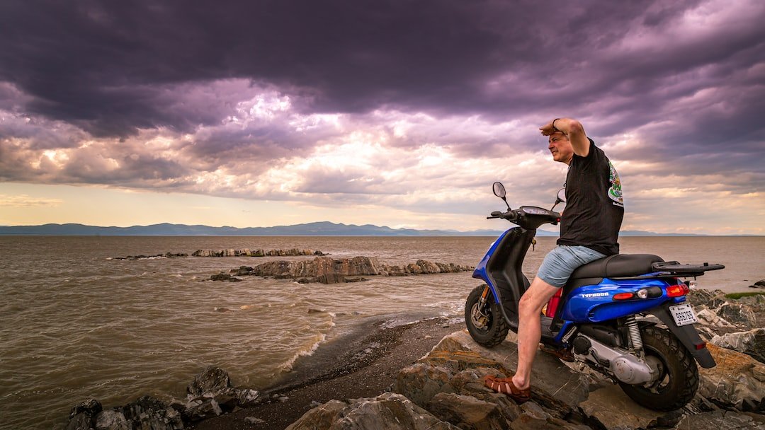 man in black jacket and blue denim jeans sitting on motorcycle on shore during daytime